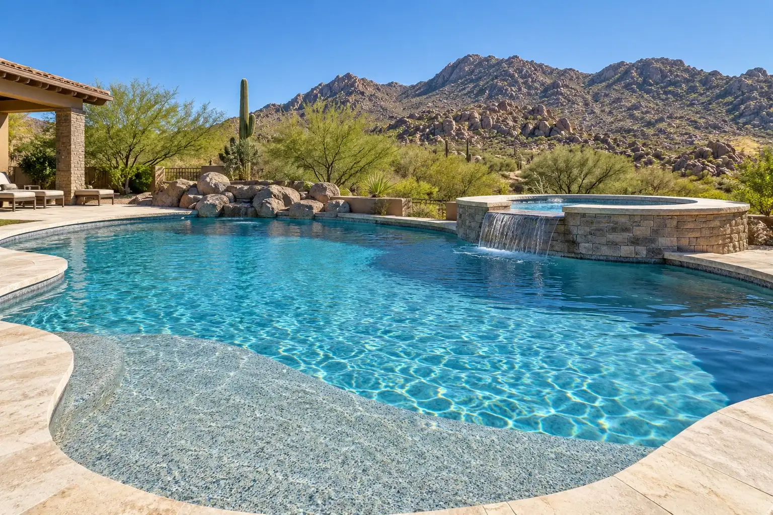 Freeform pool and raised spa with a pebble style finish below desert foothills